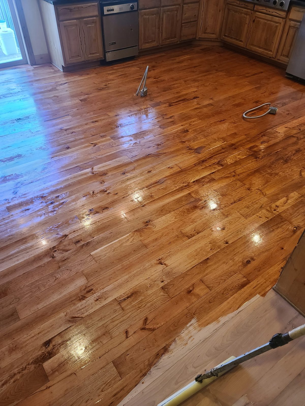 A kitchen floor with wet finish going down, ceiling lights reflecting off the fresh coat