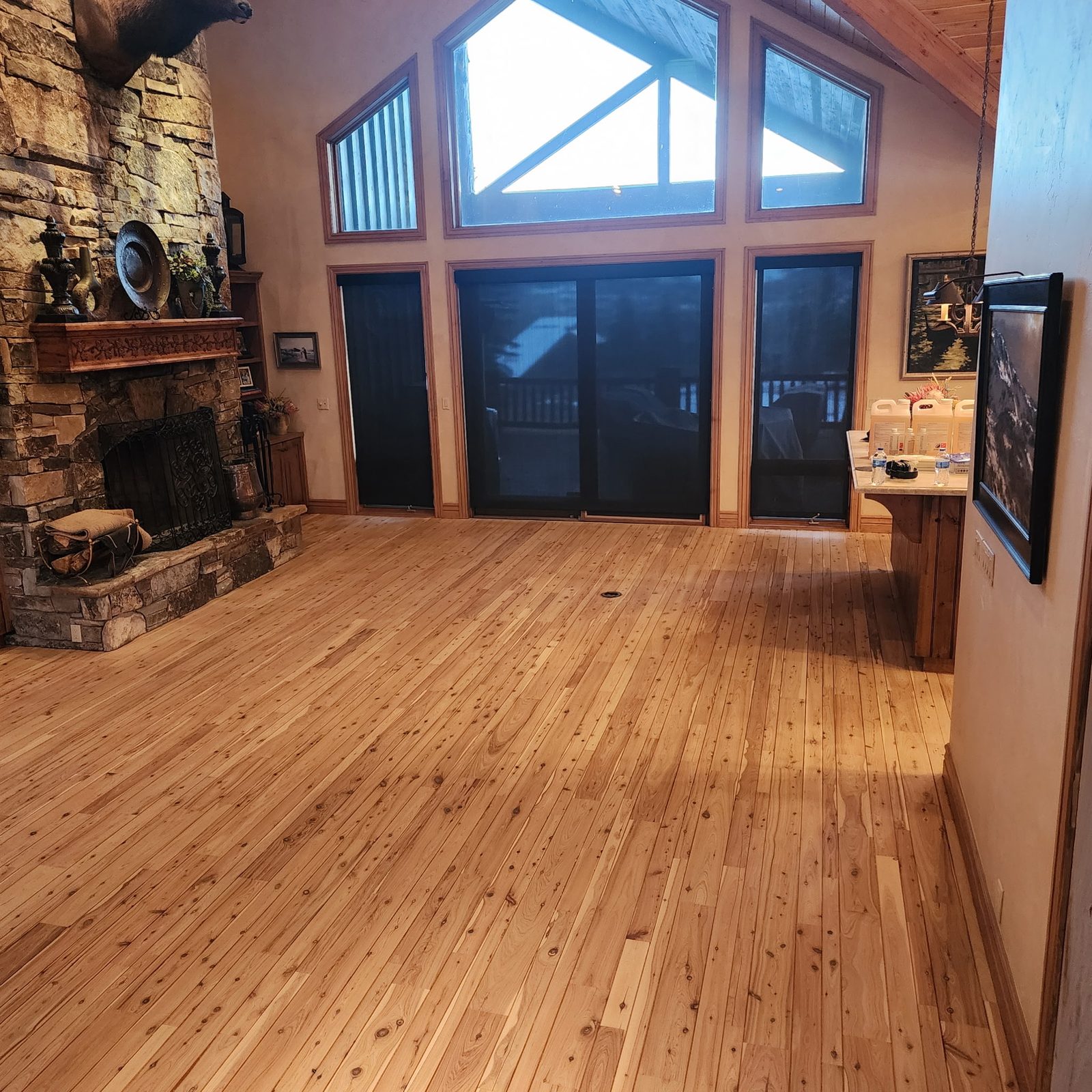 A great room with a stone fireplace and a wide, freshly finished knotty pine floor
