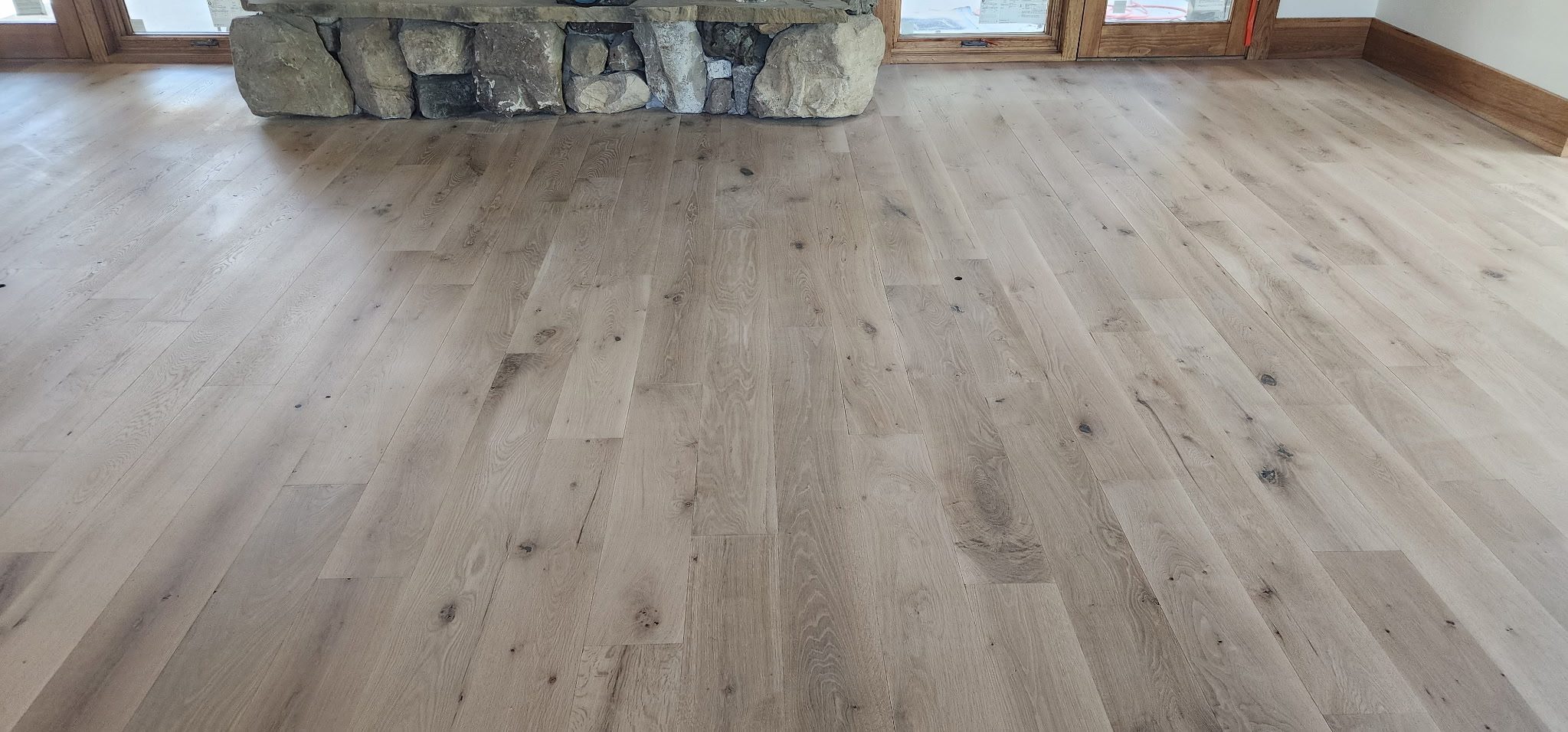 Wide-plank white oak floor finished by ADF Flooring, running toward a stone hearth