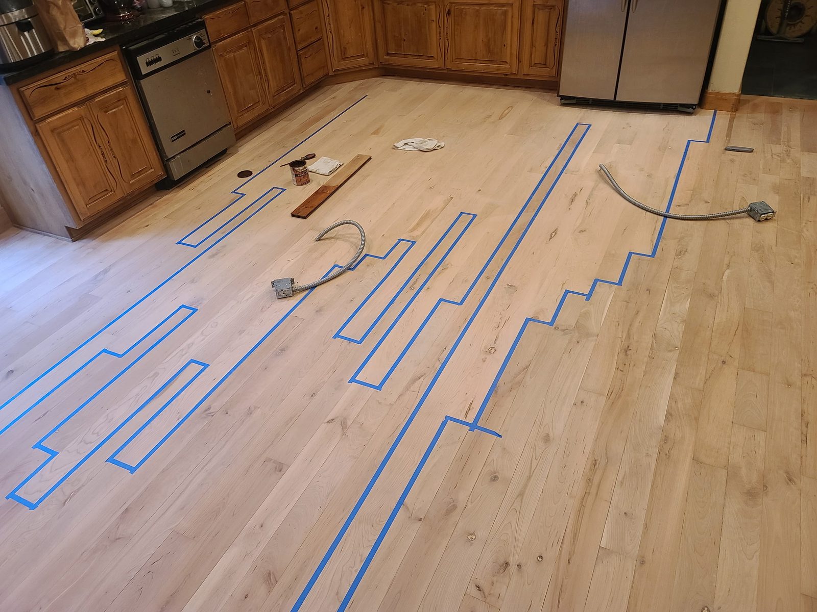A kitchen floor marked out with blue tape showing individual boards to be cut out and replaced